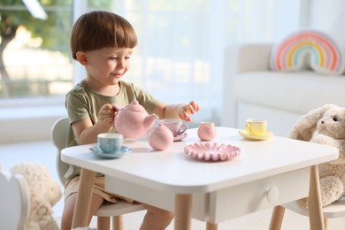 Photo of Cute little boy playing tea party with his toys at table indoors. Space for text