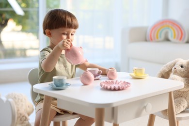 Photo of Cute little boy playing tea party with his toys at table indoors. Space for text