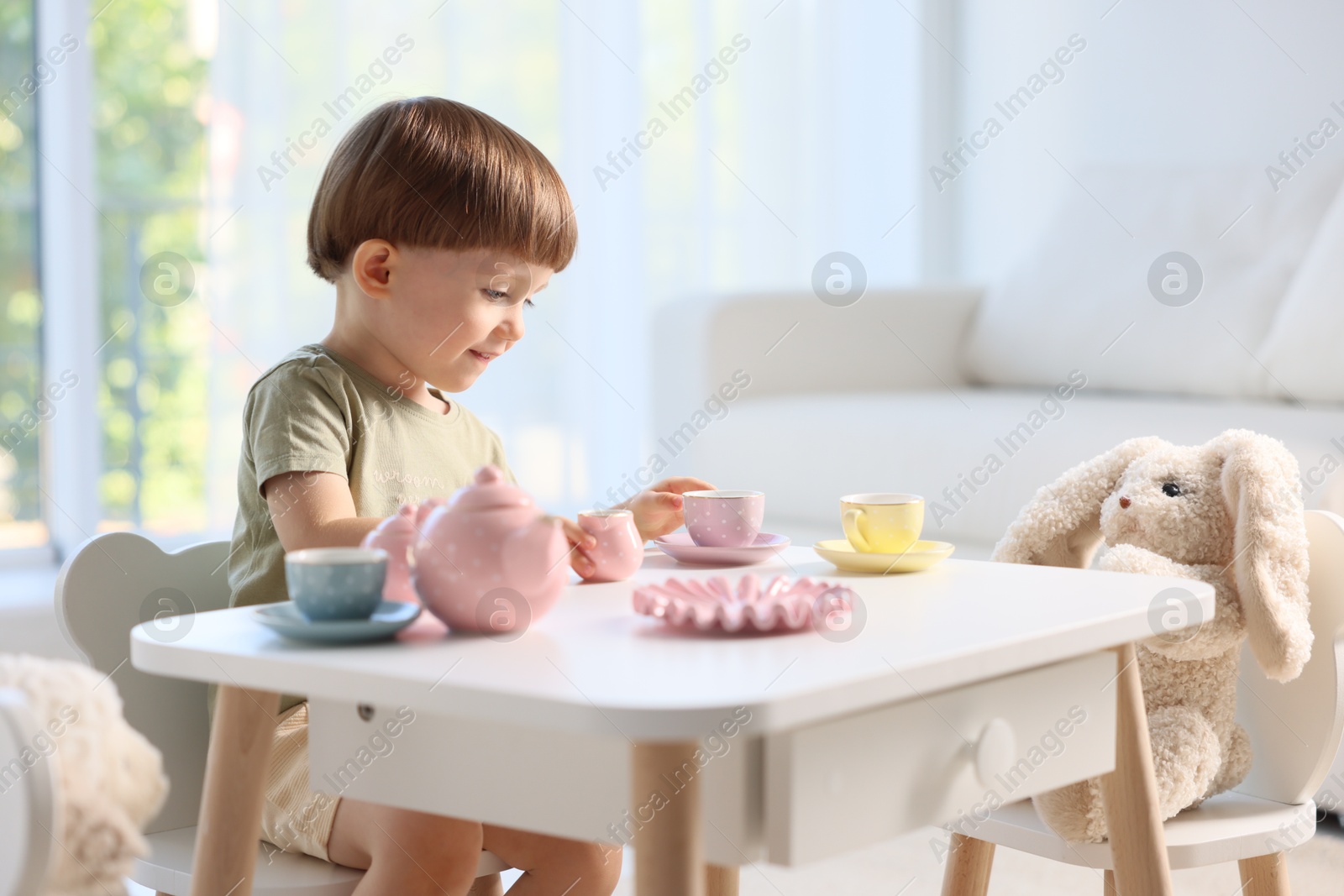 Photo of Cute little boy playing tea party with his toys at table indoors. Space for text
