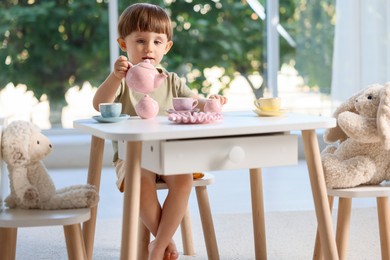 Photo of Cute little boy playing tea party with his toys at table indoors