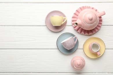 Photo of Beautiful ceramic tea set for children on white wooden table, flat lay. Space for text