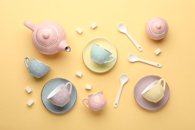 Photo of Beautiful ceramic tea set for children and sugar cubes on yellow background, flat lay