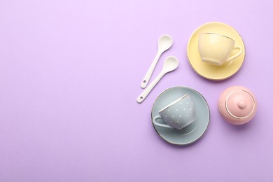Photo of Beautiful ceramic tea set for children on violet background, flat lay. Space for text