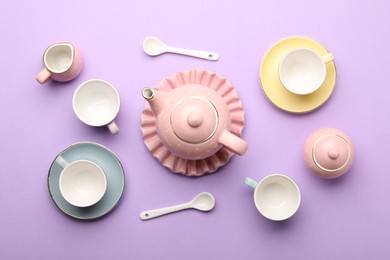 Photo of Beautiful ceramic tea set for children on violet background, flat lay