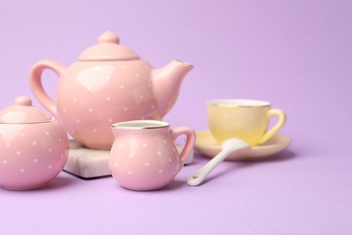 Photo of Beautiful ceramic tea set for children on violet background, closeup