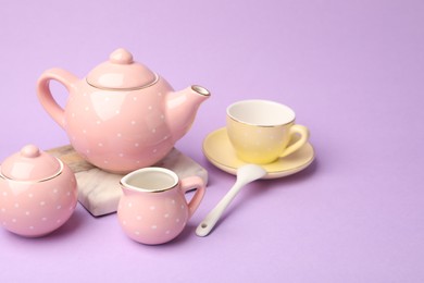 Photo of Beautiful ceramic tea set for children on violet background, closeup. Space for text