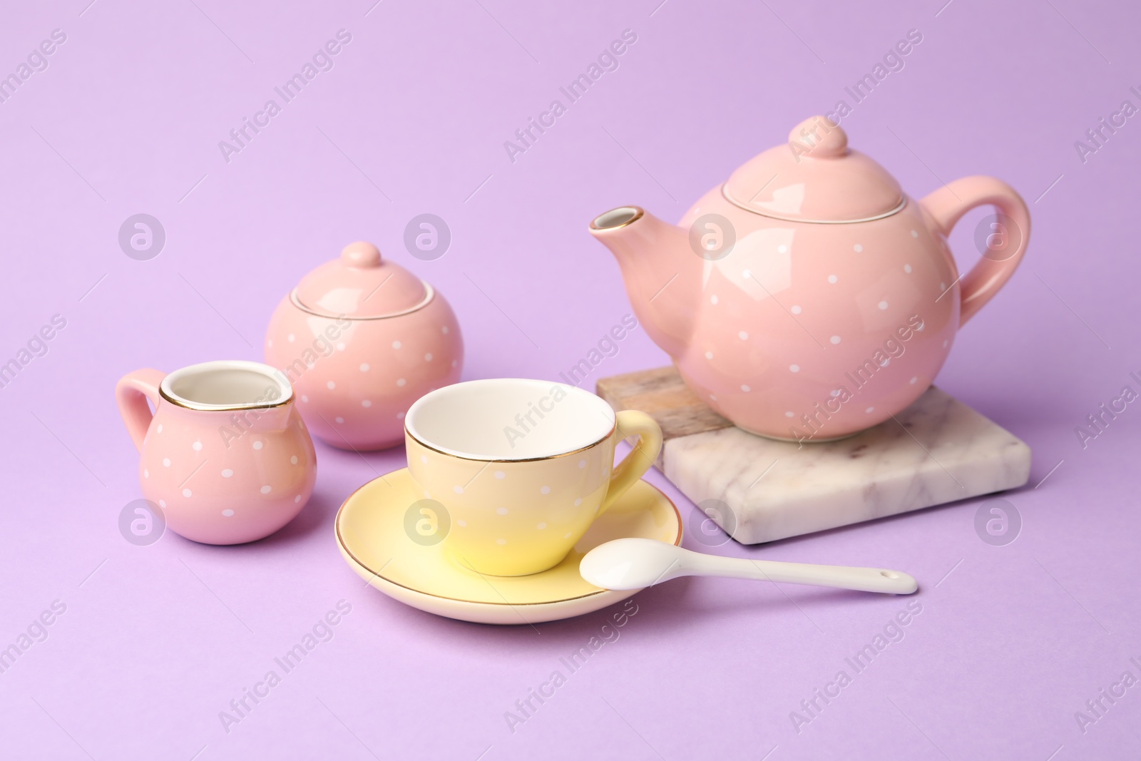 Photo of Beautiful ceramic tea set for children on violet background, closeup