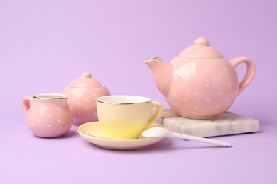Photo of Beautiful ceramic tea set for children on violet background, closeup