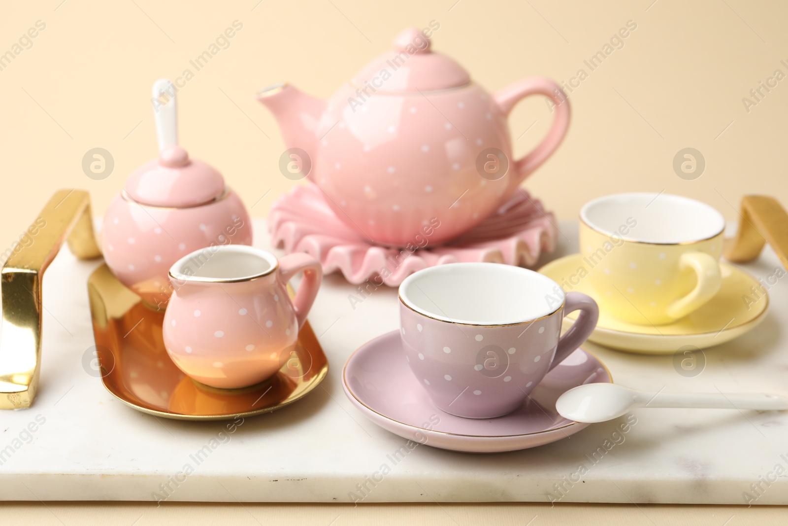 Photo of Tray with beautiful ceramic tea set for children on beige background, closeup