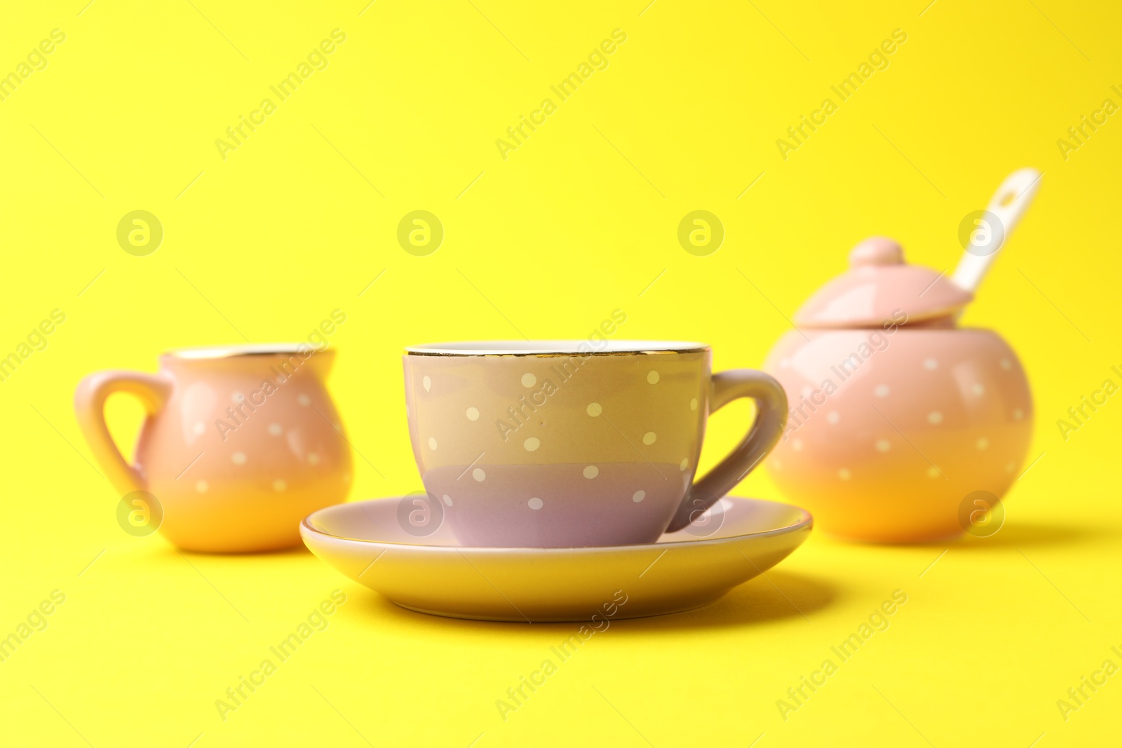Photo of Beautiful ceramic tea set for children on yellow background, closeup