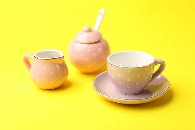 Photo of Beautiful ceramic tea set for children on yellow background, closeup