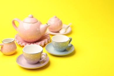 Photo of Beautiful ceramic tea set for children on yellow background, closeup. Space for text
