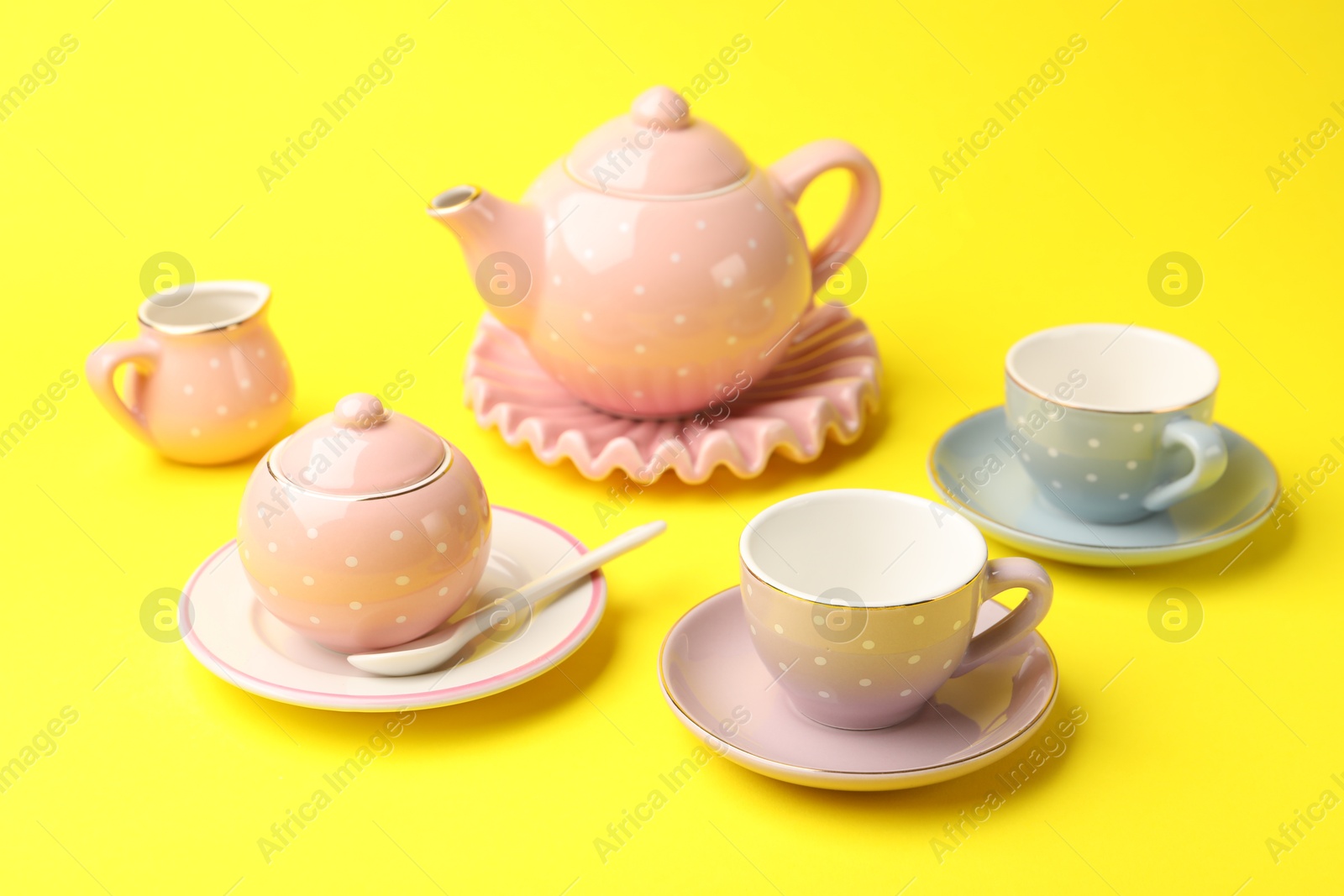 Photo of Beautiful ceramic tea set for children on yellow background, closeup