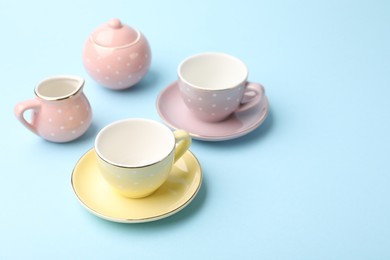 Photo of Beautiful ceramic tea set for children on light blue background, closeup. Space for text