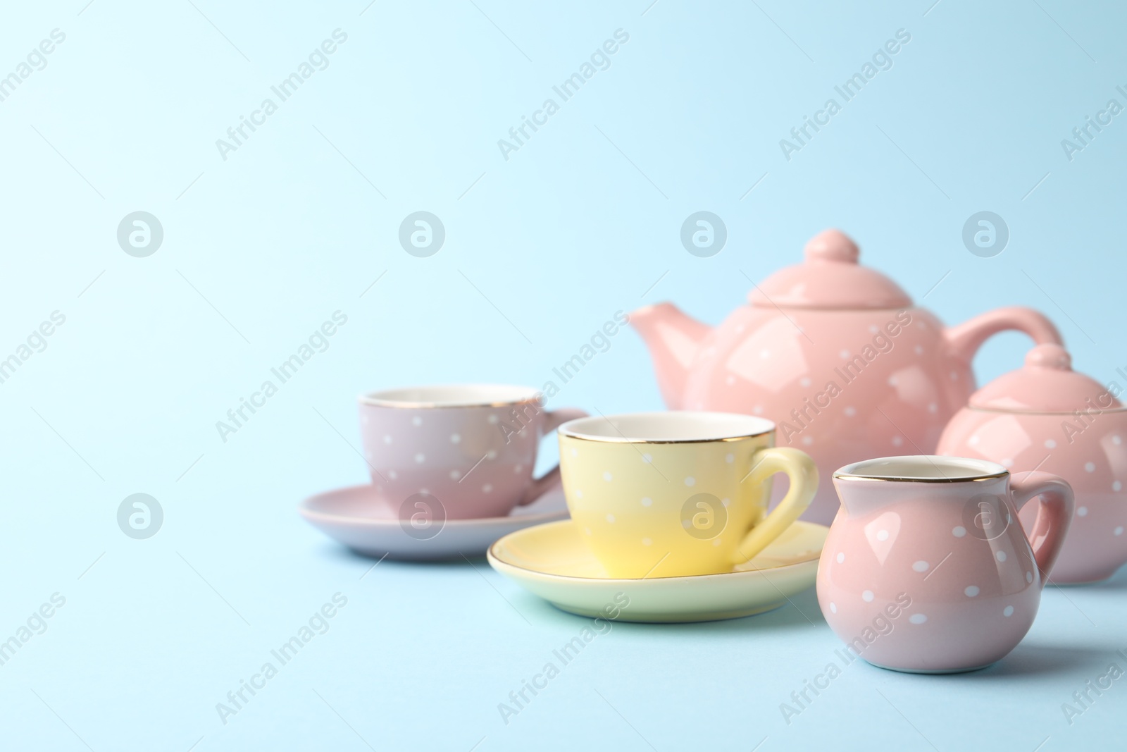 Photo of Beautiful ceramic tea set for children on light blue background, closeup. Space for text