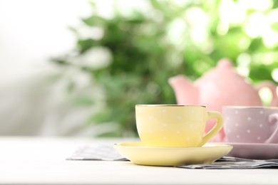 Photo of Ceramic tea set for children. Beautiful cups and teapot on white wooden table against blurred background, closeup with space for text