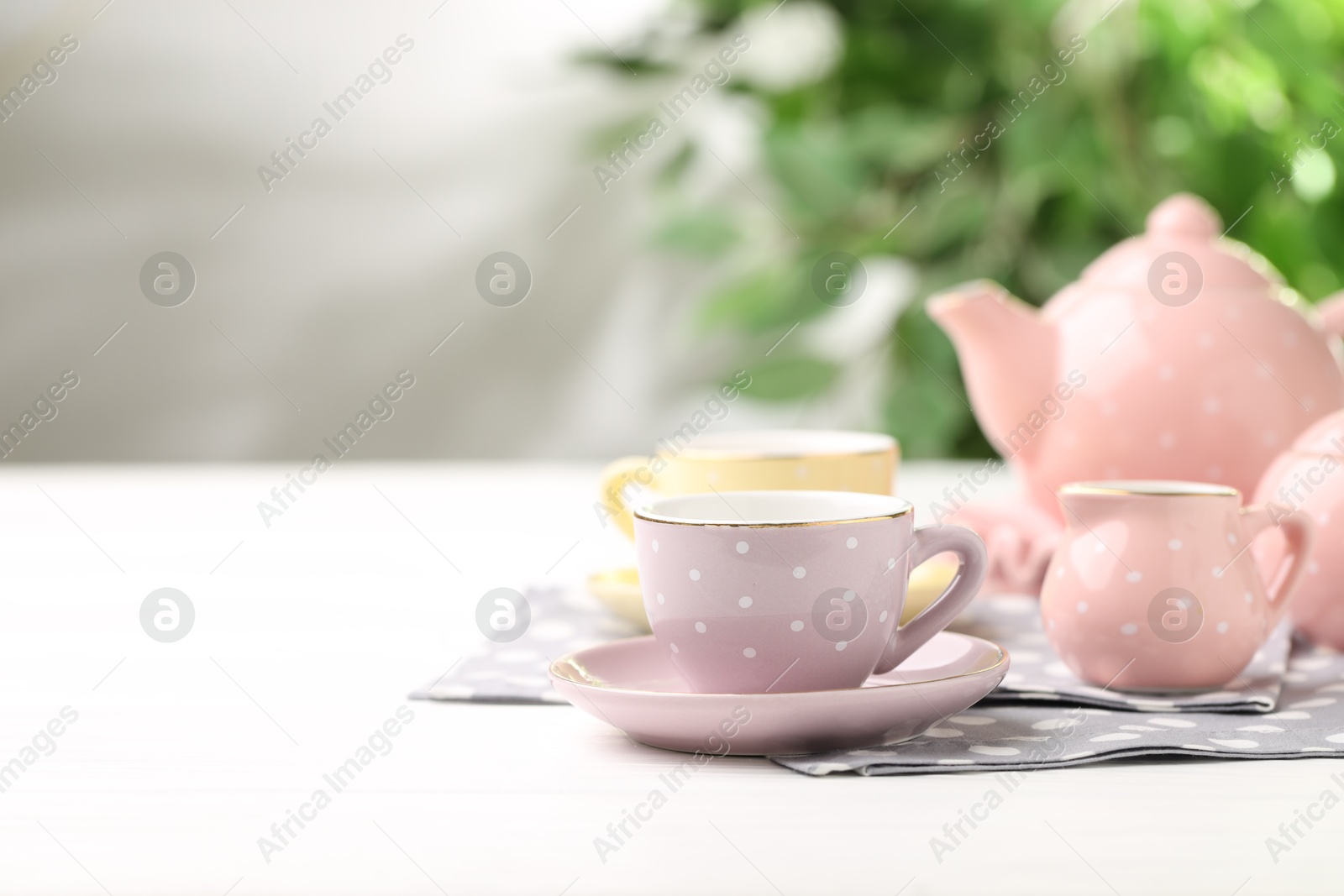 Photo of Beautiful ceramic tea set for children on white wooden table against blurred background, closeup. Space for text