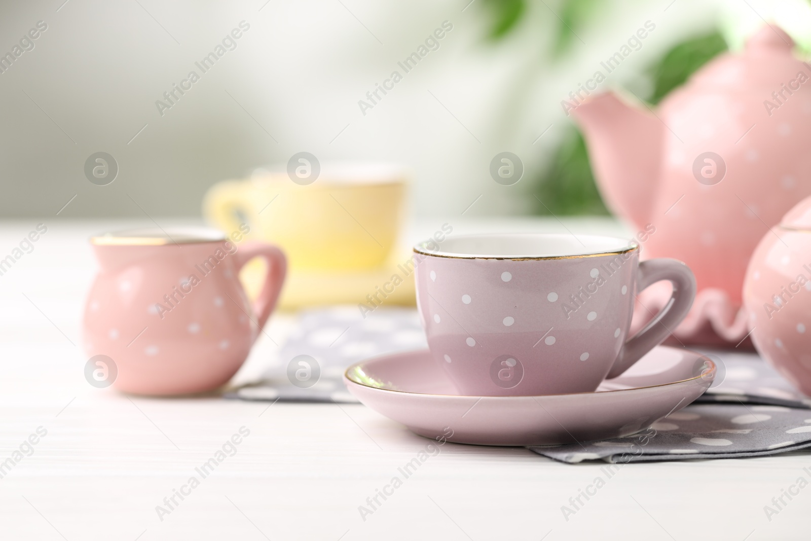 Photo of Beautiful ceramic tea set for children on white wooden table against blurred background, closeup
