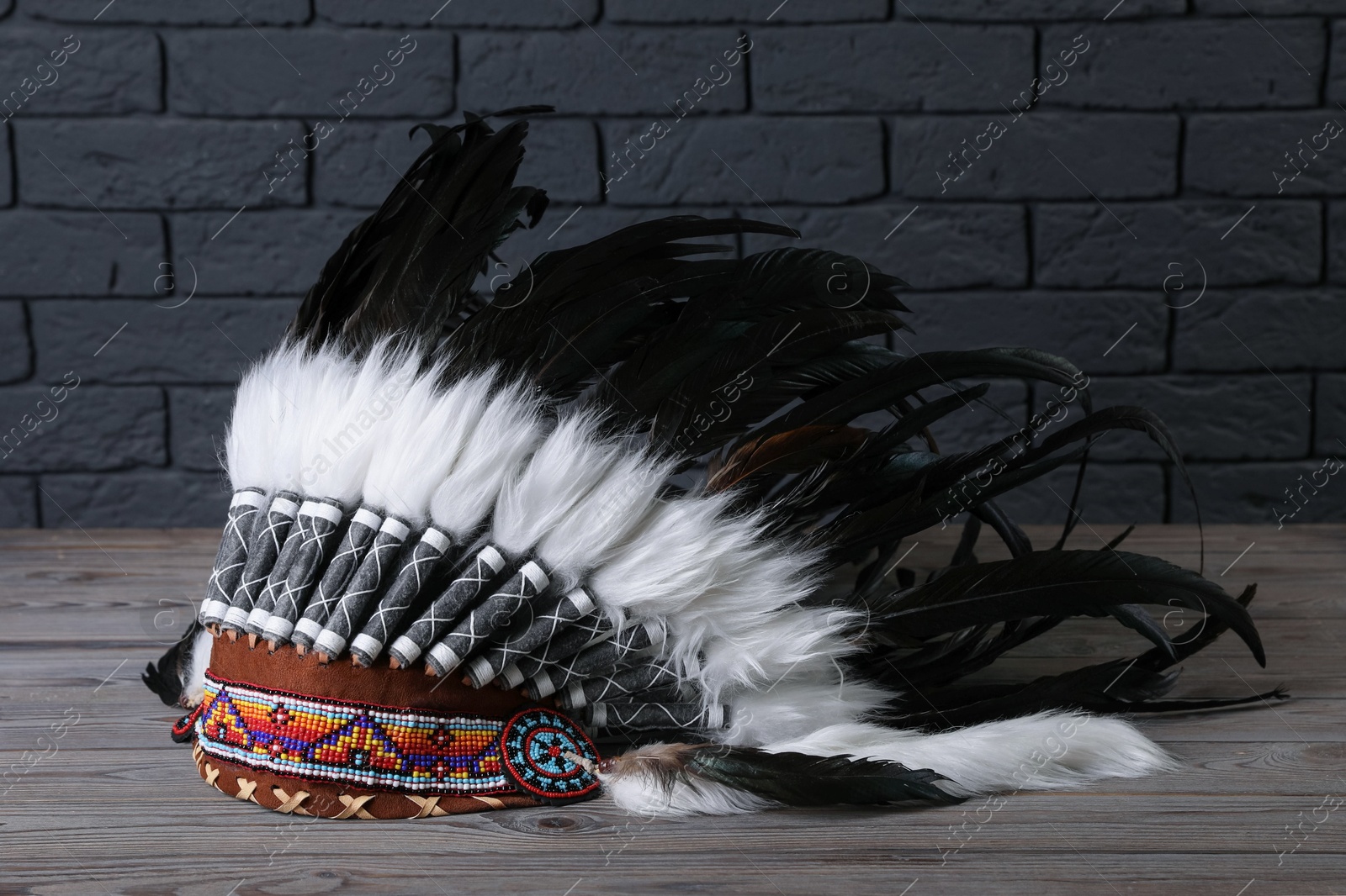 Native American chief headdress (feathered war bonnet) on wooden surface against gray brick wall Photo of Native American chief headdress (feathered war bonnet) on wooden surface against gray brick wall