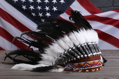 Photo of Native American chief headdress (feathered war bonnet) on wooden surface against American flag