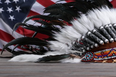Photo of Native American chief headdress (feathered war bonnet) on wooden surface against American flag, closeup