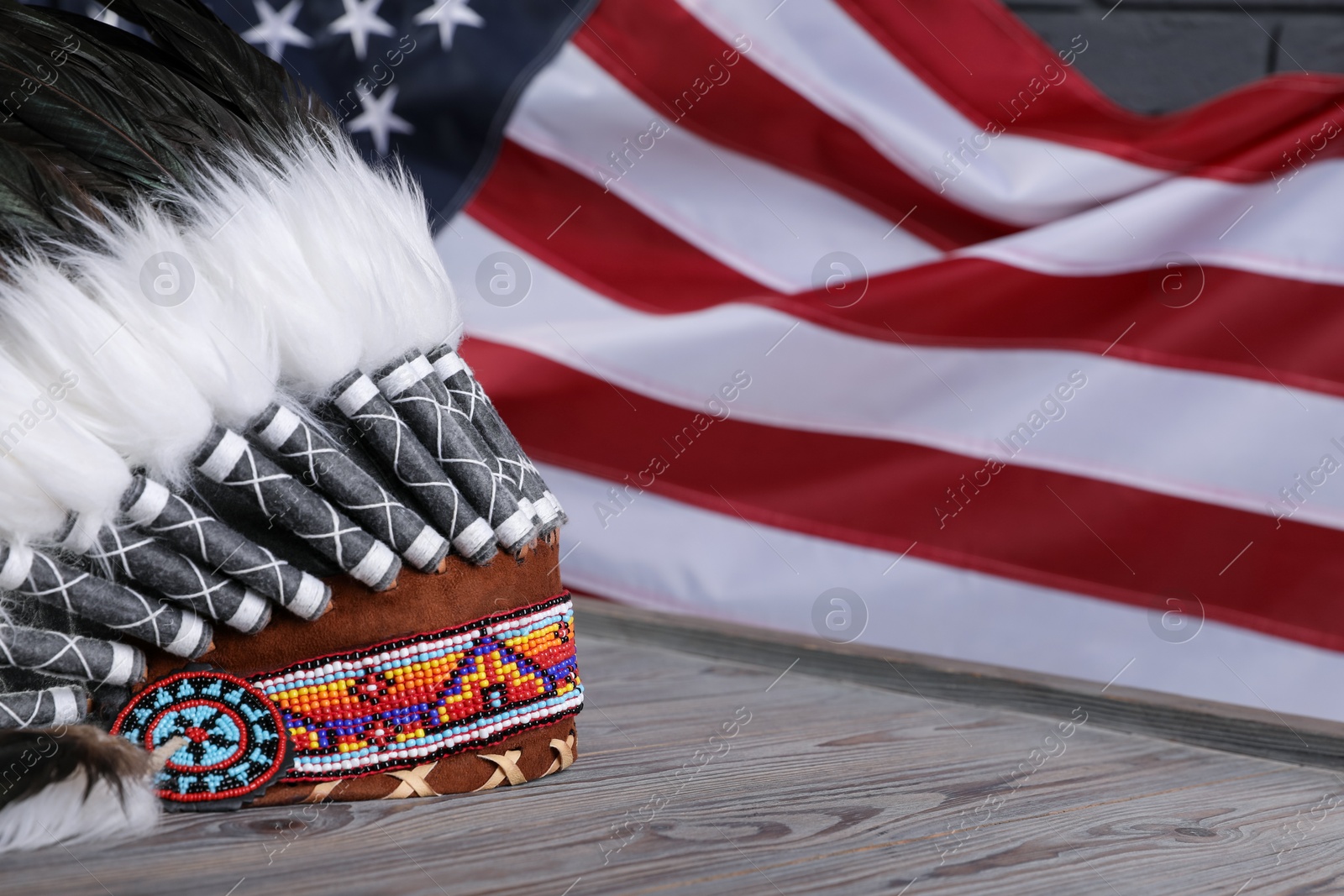 Native American chief headdress (feathered war bonnet) on wooden surface against American flag, closeup. Space for text Photo of Native American chief headdress (feathered war bonnet) on wooden surface against American flag, closeup. Space for text