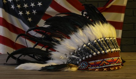 Photo of Native American chief headdress (feathered war bonnet) on wooden surface against American flag in color light