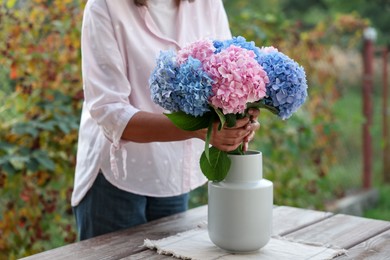 Photo of Senior woman putting beautiful bouquet of flowers into vase in garden, closeup