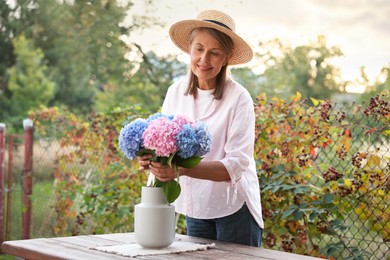 Photo of Senior woman putting beautiful bouquet of flowers into vase in garden