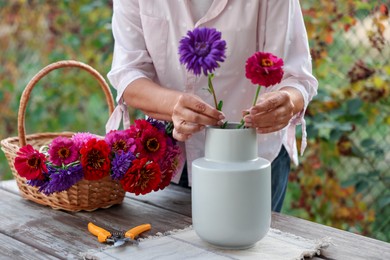 Photo of Senior woman making beautiful bouquet of flowers at wooden table in garden, closeup