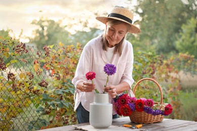 Photo of Senior woman making beautiful bouquet of flowers at wooden table in garden