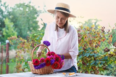 Photo of Senior woman making beautiful bouquet of flowers at wooden table in garden