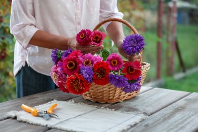 Photo of Senior woman making beautiful bouquet of flowers at wooden table in garden, closeup