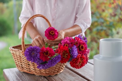 Photo of Senior woman making beautiful bouquet of flowers at wooden table in garden, closeup