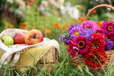 Photo of Beautiful bouquet of flowers in wicker basket and apples on green grass outdoors, closeup