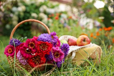 Photo of Beautiful bouquet of flowers in wicker basket and apples on green grass outdoors, closeup