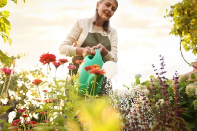 Photo of Senior woman watering beautiful flowers with can in garden, low angle view