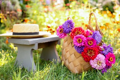 Photo of Bouquet of flowers in bag, stool and wicker hat on green grass outdoors