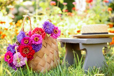 Photo of Bouquet of flowers in bag, stool and wicker hat on green grass outdoors