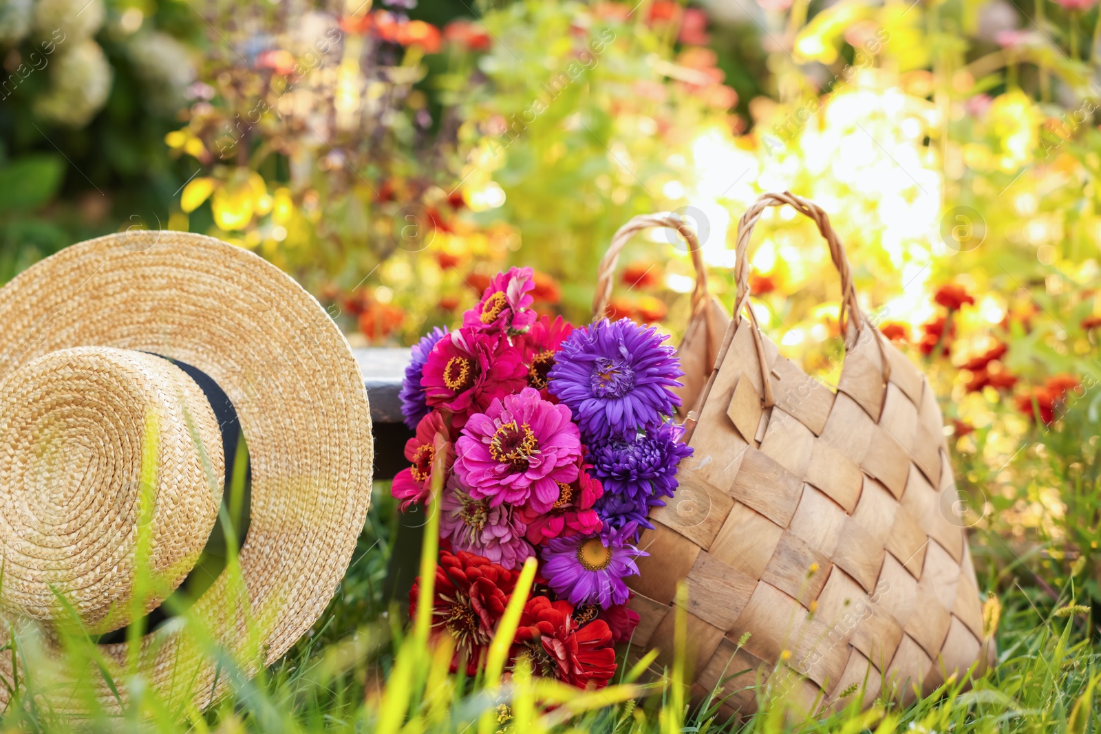 Photo of Bouquet of flowers in bag and wicker hat on green grass outdoors