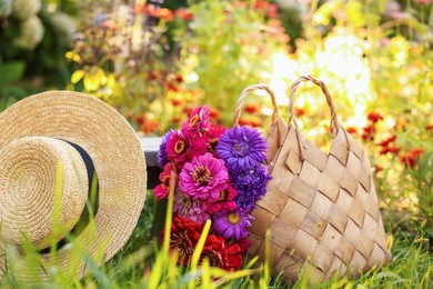 Photo of Bouquet of flowers in bag and wicker hat on green grass outdoors