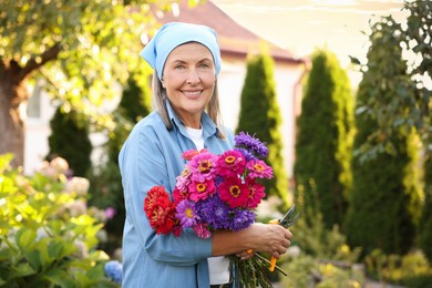 Photo of Senior woman with bouquet of flowers and pruner in garden