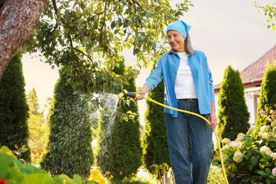 Photo of Senior woman watering beautiful flowers with hose in garden, low angle view