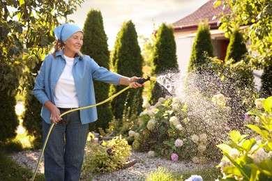 Photo of Senior woman watering beautiful flowers with hose in garden