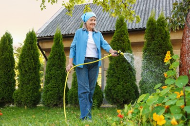 Photo of Senior woman watering beautiful flowers with hose in garden
