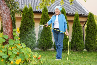 Photo of Senior woman watering beautiful flowers with hose in garden