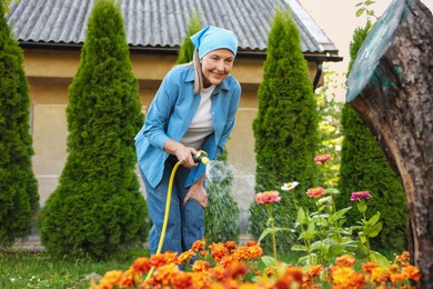 Photo of Senior woman watering beautiful flowers with hose in garden