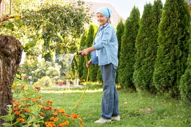 Photo of Senior woman watering beautiful flowers with hose in garden