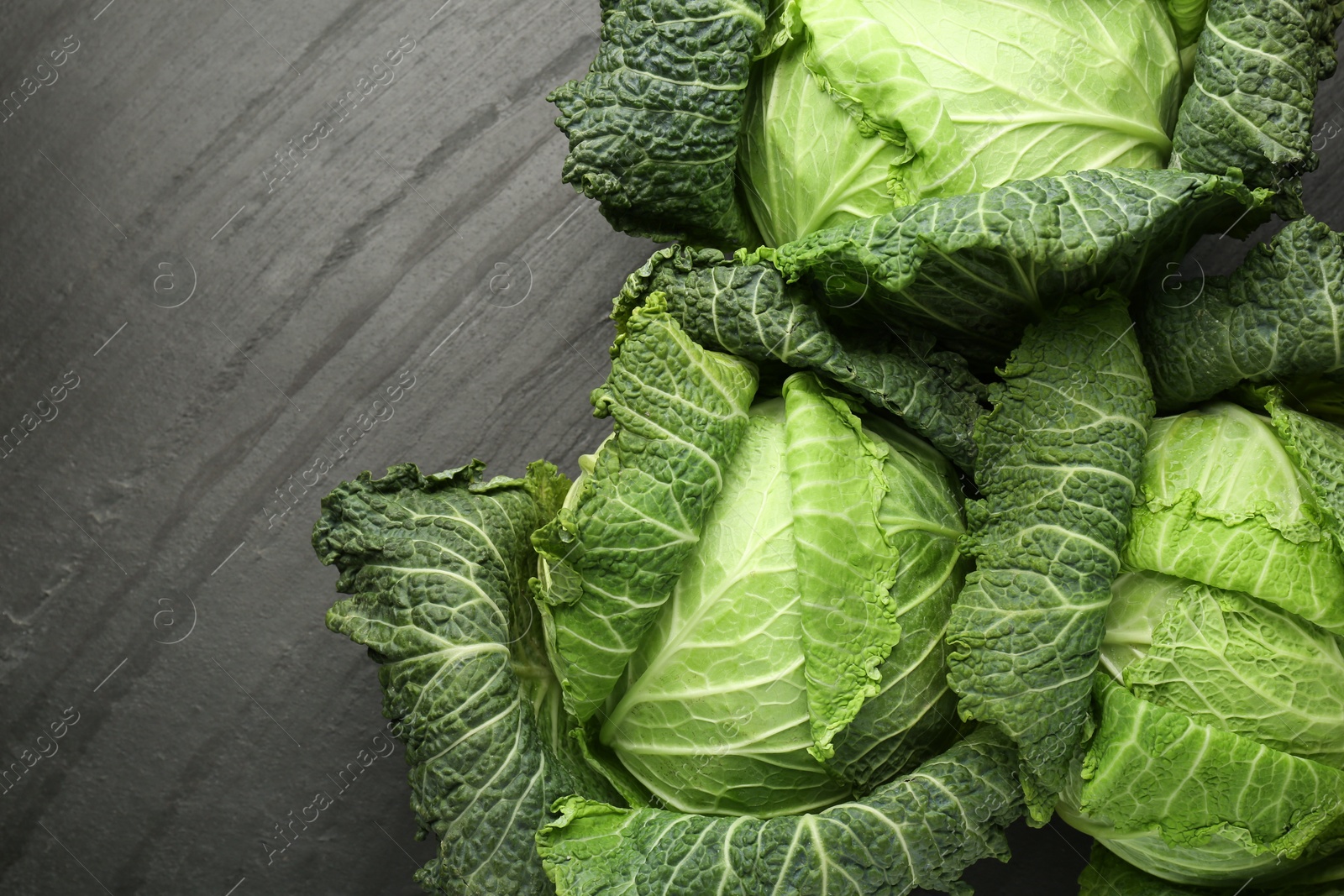 Photo of Fresh Savoy cabbages on black textured table, flat lay. Space for text