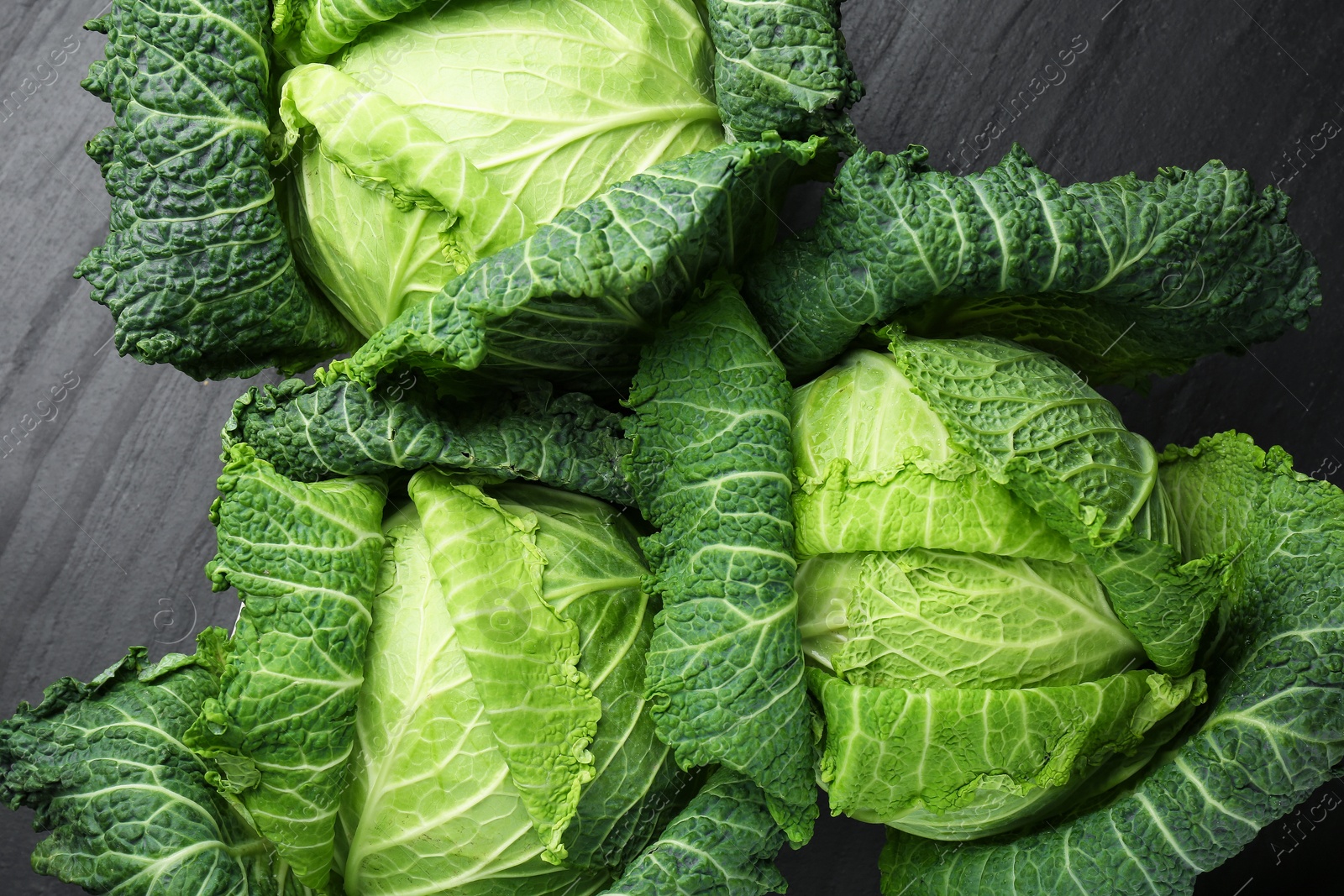 Photo of Fresh Savoy cabbages on black textured table, flat lay